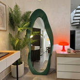 Modern interior with a green floor mirror, plants, and a red lamp.